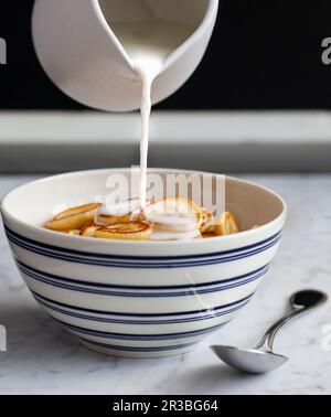 Il latte viene versato in un recipiente blu e bianco di mini pancake (cereali per frittelle dolci) Foto Stock