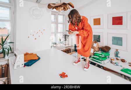 Stilista che fotografa il prodotto in piedi sul banco di lavoro Foto Stock