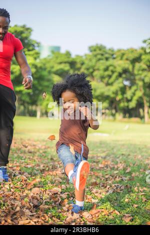 Figlio che calcia le foglie secche con il padre al parco Foto Stock