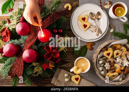 Una accesa corona d'avvento accanto a un piatto di biscotti, caffè e tè Foto Stock