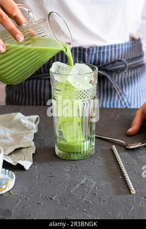 La donna versa il tè Matcha in un bicchiere con cubetti di ghiaccio Foto Stock