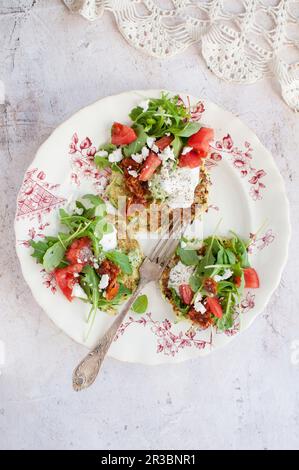 Tortine di zucchine ricoperte di panna, pomodoro, rucola e feta Foto Stock