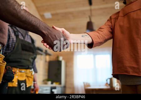 Primo piano della giovane casalinga che scuote la mano dell'idraulico afroamericano dopo aver riparato il tubo o qualcos'altro contro l'interno della cucina Foto Stock