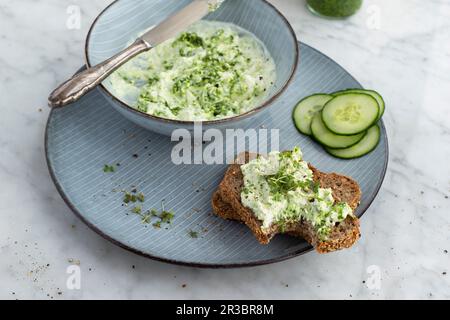 Crema di formaggio di pecora all'aglio selvatico su pane integrale con fettine di cetriolo Foto Stock