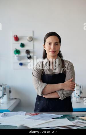 Giovane donna di successo conciatore in abbigliamento da lavoro in piedi dal posto di lavoro in studio di lavorazione del cuoio e guardare la macchina fotografica durante il lavoro Foto Stock