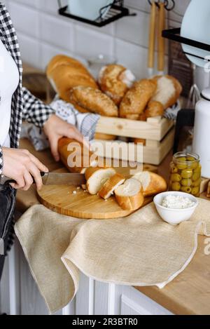 Donna in cucina fa sandwich da baguette e formaggio cremoso Foto Stock