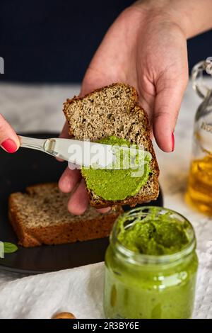 Spalmare il pesto di basilico e rucola fatti in casa in un vasetto su un pezzo di pane Foto Stock