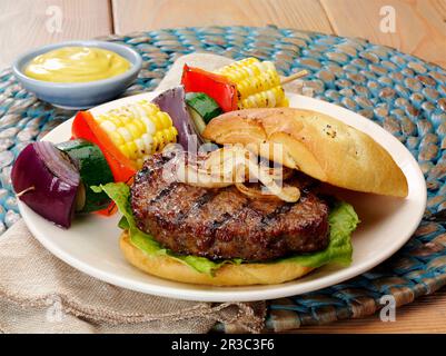 Hamburger di maiale macinato alla griglia con cipolle grigliate su un panino di ciabatta e spiedino di verdure Foto Stock