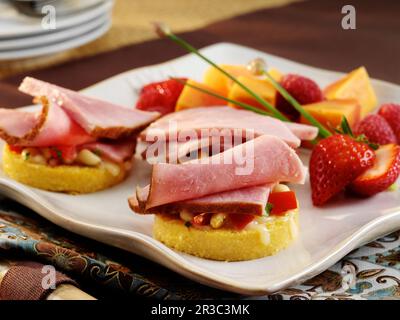 Antipasti di crostini al prosciutto con pomodoro, verdure e mozzarella su rotonde di pane di mais Foto Stock