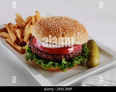 Hamburger con lattuga, pomodoro e cipolla su un panino di semi di sesamo con patatine fritte e un sottaceto di aneto intero Foto Stock