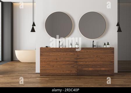 Bagno interno luminoso con pavimento in parquet, doppio lavabo beige, lavandino in legno, vasca beige, wc e specchi ovali, grande finestra. Accogliente b minimalista Foto Stock