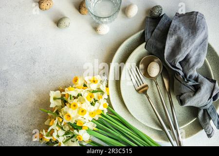 Ambiente per la cena di Pasqua con fiori di daffodil e uova su sfondo di cemento Foto Stock