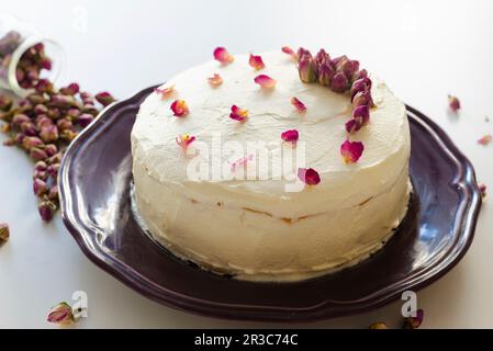 Torta di rose decorata con boccioli di rosa secchi e petali su un piatto viola Foto Stock