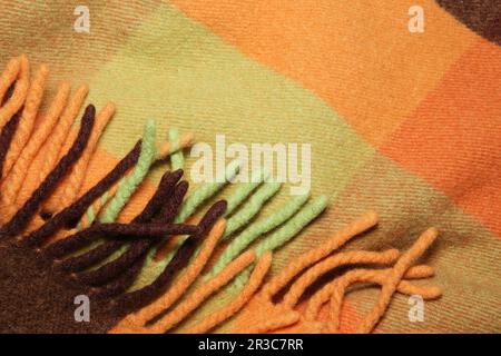 Coperta morbida e calda in lana d'alpaca ripiegata con frangia. Macrofo a trama di lana verde e arancione Foto Stock