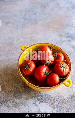 Pomodori di vite organici in colino di ceramica giallo Foto Stock