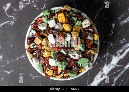 Pietre colorate caramelle al cioccolato. Drago di cioccolato in pietra in ciotola di ceramica su sfondo scuro. Piccole caramelle multicolore. Vista dall'alto Foto Stock