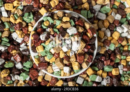 Pietre colorate caramelle al cioccolato. Drago di cioccolato in pietra in ciotola di ceramica. Piccole caramelle multicolore. Vista dall'alto Foto Stock