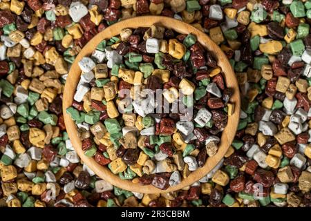 Pietre colorate caramelle al cioccolato. Drago di cioccolato in pietra in ciotola di legno. Piccole caramelle multicolore. Vista dall'alto Foto Stock