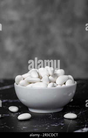 Caramelle alle mandorle. Caramella di mandorle ricoperta di zucchero in ciotola di ceramica su fondo scuro. Piccole caramelle multicolore Foto Stock