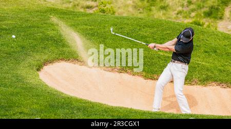 Uomo che colpisce la sfera di golf da un bunker Foto Stock