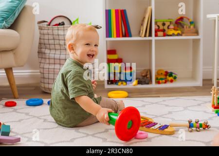 Il bambino felice sta giocando con i giocattoli differenti nella stanza dei bambini Foto Stock