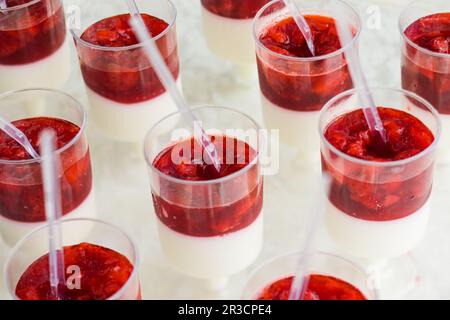 La porzione di primo piano dei dessert panna cotta con fragole. Dessert italiano in tazze di plastica su un tavolo di legno bianco Foto Stock