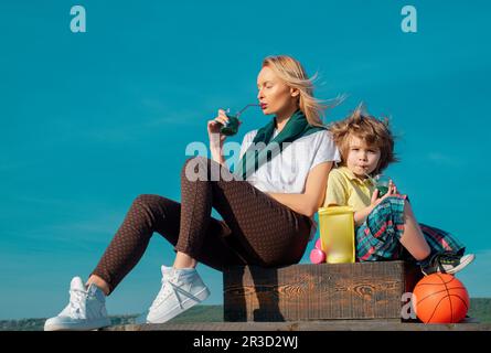 Madre e figlio si rilassano dopo lo sport. Giovane donna con bambino che indossa abiti sportivi che bevono frullato dopo l'allenamento all'aperto. Bevanda proteica per la salute. Foto Stock