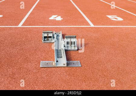 Superficie della pista di corsa con texture rosse con un blocco di partenza davanti alla linea di partenza numero quattro, primo piano a livello del suolo. Foto Stock