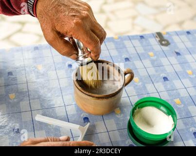 Mani più anziane utilizzando la spazzola di rasatura con la lama sul tavolo blu Foto Stock