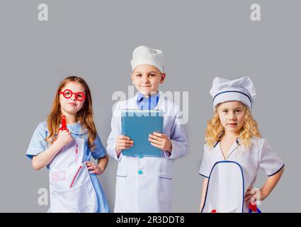 Carino bambini vestiti come medici su grigio Foto Stock