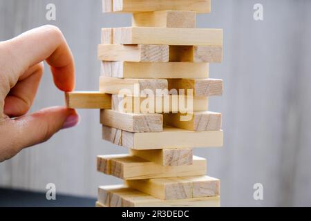 Edificio da blocchi di legno. Gioco per famiglia di bar in legno. Legno blocchi stack gioco con mano sullo sfondo. Blocco torre con ar Foto Stock