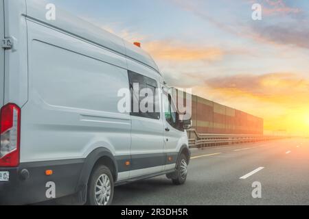 Mini furgone bianco guida lungo l'autostrada in lontananza sullo sfondo del cielo serale Foto Stock