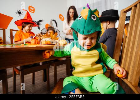 Bambino piccolo in costume fantasia verde seduto e piangendo Foto Stock