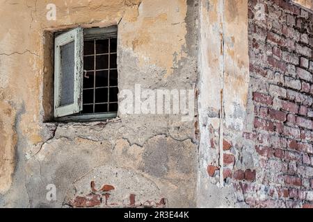 Piccola finestra di legno barrata. Immagine vintage con il vecchio muro di mattoni logoro di un edificio abbandonato. Foto Stock