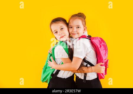 Due studentesse sorridenti in uniforme stanno abbracciando il giallo Foto Stock