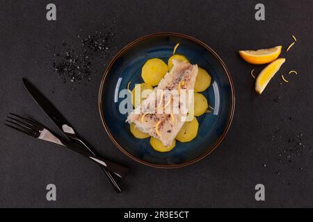 Filetto di pesce alla griglia servito con patate sul piatto su sfondo nero. Foto Stock