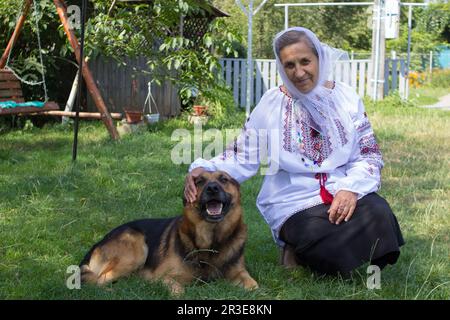 la donna di pensione si siede con il cane sull'erba in camicia ricamata Foto Stock