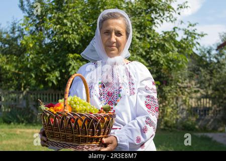 la nonna tiene un cesto pieno di frutta in una blusa ricamata Foto Stock