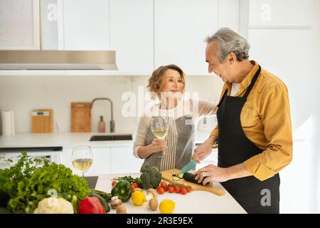 Sposi anziani amorevoli che celebrano l'anniversario del matrimonio, parlano, fanno la cena e bevono vino da donna Foto Stock