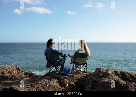 Felice giovane coppia seduta in sedie da campeggio su Beach Rocks vicino Ocean Foto Stock