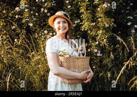 Bella donna in cappello che tiene il cesto con fiori Foto Stock