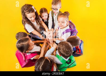 Gli scolari stanno accatastando le mani insieme sullo sfondo giallo Foto Stock