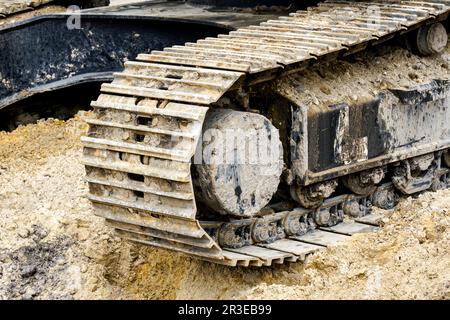 Escavatore cingolato fangoso e sabbioso, cingoli metallici sporchi con ruote in acciaio pieno in primo piano. Telaio dei veicoli cingolati Foto Stock