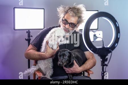 Radio host, affascinante influencer, registra uno spettacolo dal vivo con materiale e attrezzature per la fotocamera. Cani bianchi e neri. Monolocale colorato. Foto Stock