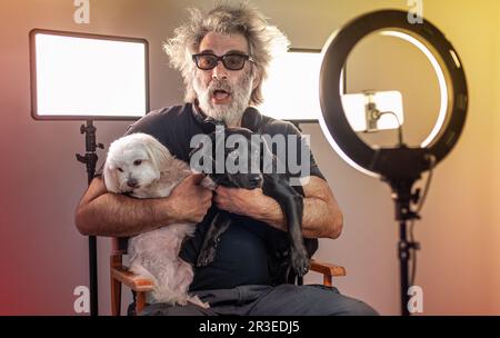 Radio host, affascinante influencer, registra uno spettacolo dal vivo con materiale e attrezzature per la fotocamera. Cani bianchi e neri. Monolocale colorato. Foto Stock