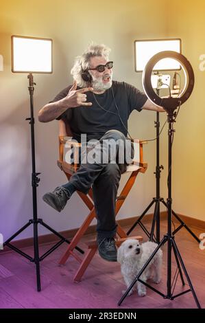 Radio host, affascinante influencer, registra uno spettacolo dal vivo con materiale e attrezzature per la fotocamera. Cani bianchi e neri. Monolocale colorato. Foto Stock