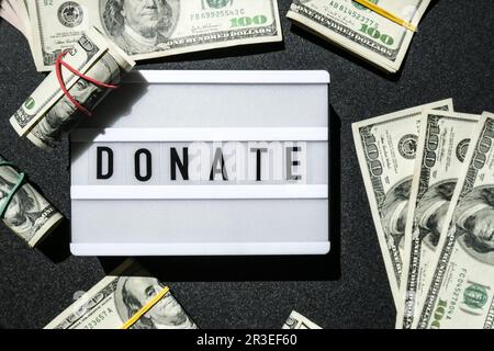 Cartone luminoso con parole DONATE in lettere nere intorno alle banconote in dollari USA. Soldi, affari, finanza, investimento, risparmio Foto Stock