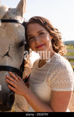 Ritratto di una giovane donna in abito bianco che abbraccia il cavallo Foto Stock