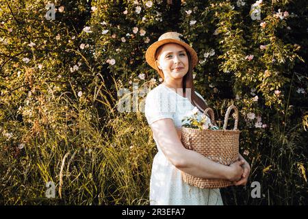 Bella donna in cappello che tiene il cesto con fiori Foto Stock