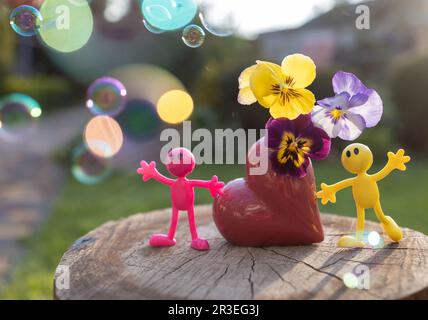 Statuette giocattolo in miniatura di persone vicino a un vaso a forma di cuore con pannelli e bolle splendidamente illuminate dal sole Foto Stock